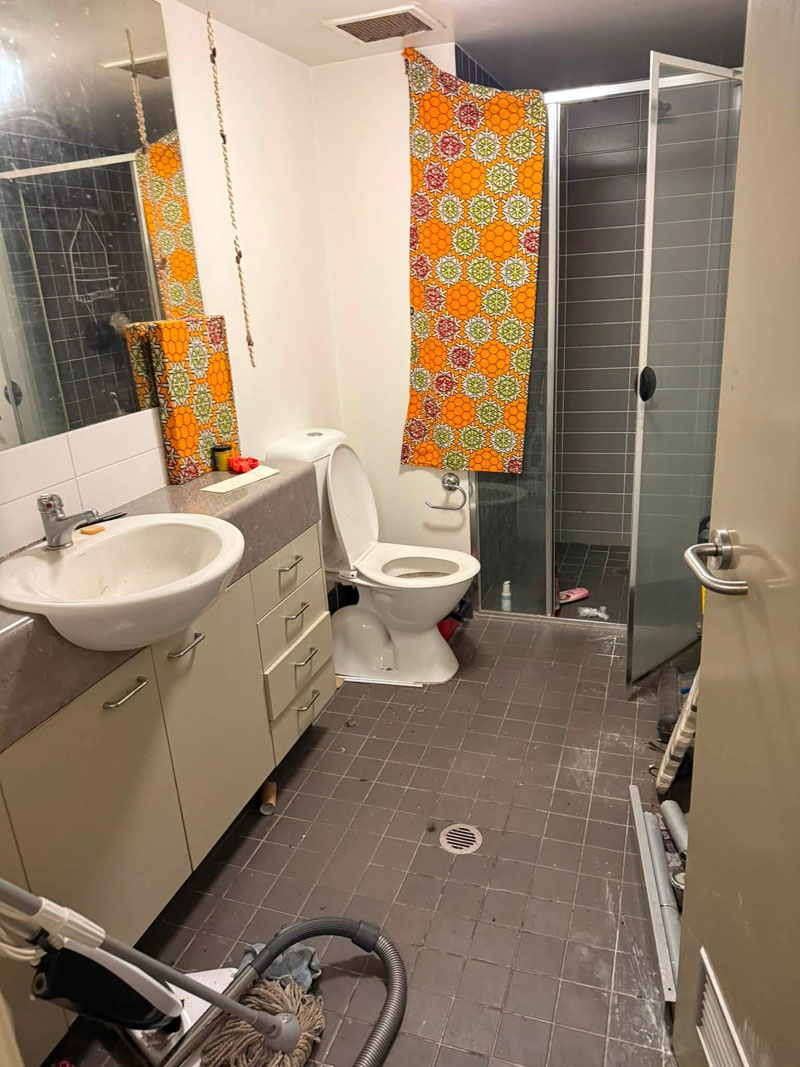 Bathroom with grey floor tiles, vanity, toilet and shower, a vacuum in the doorway
