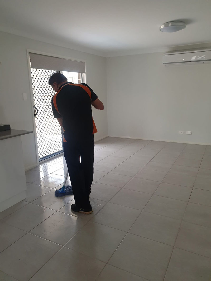 Cleaner mopping a tiled floor in an empty living area