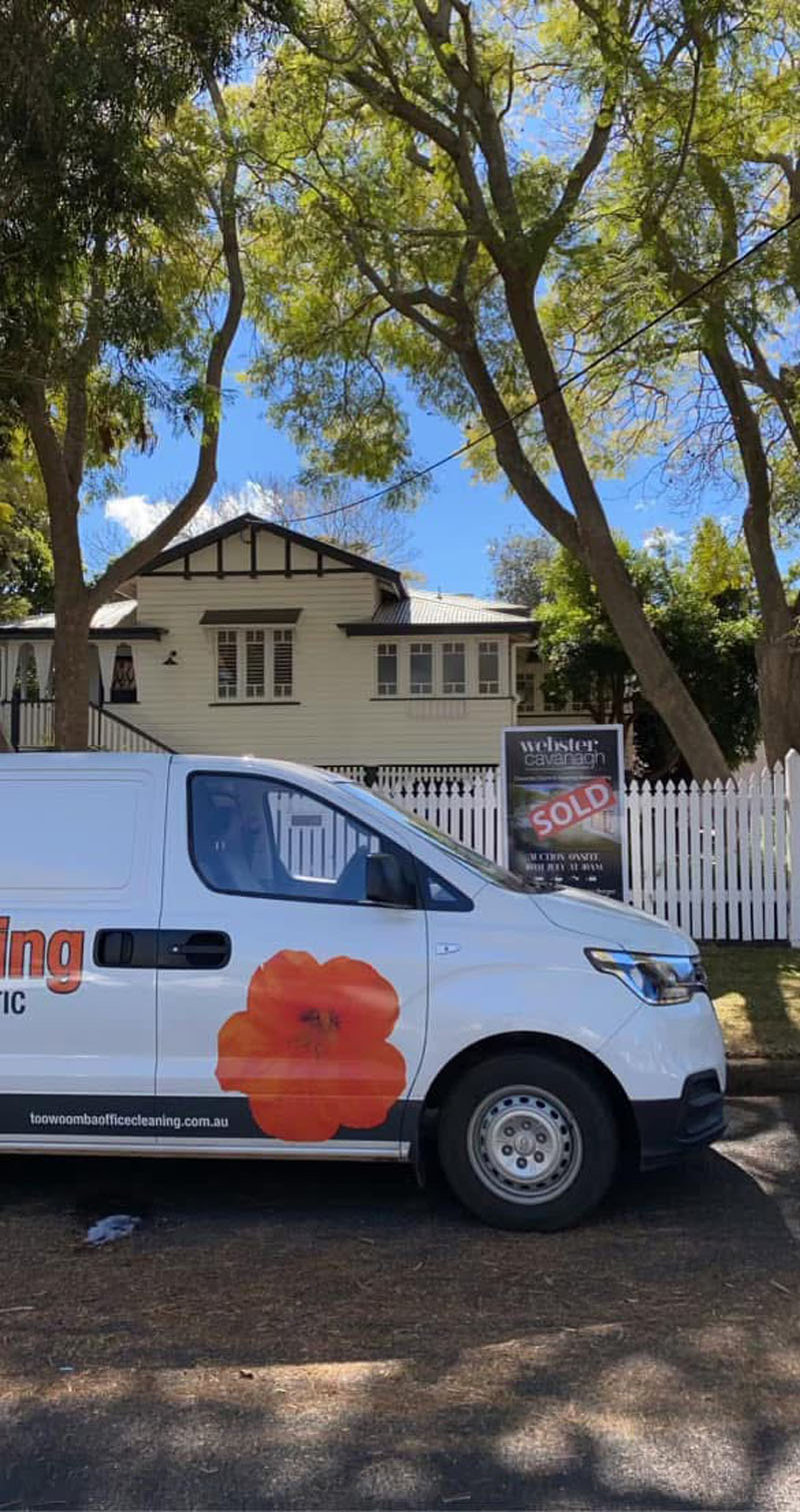 White work van with an orange flower logo parked outside a weatherboard house