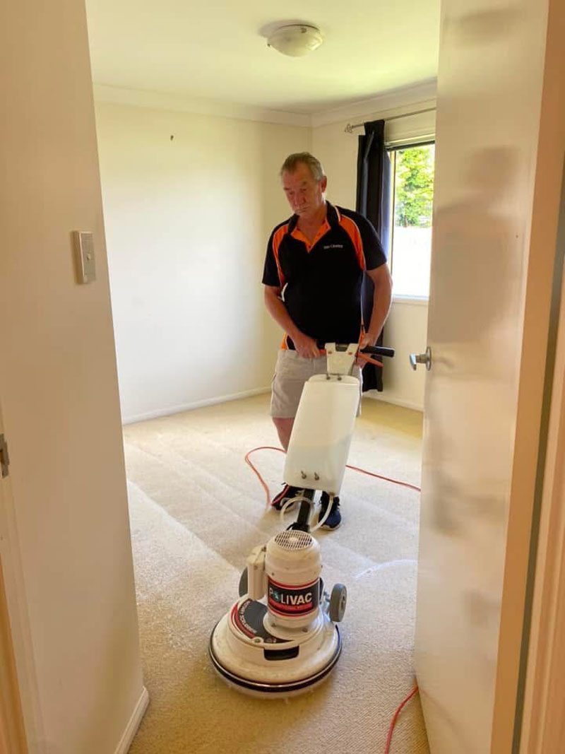 Cleaner using a rotary floor machine on carpet in an empty bedroom