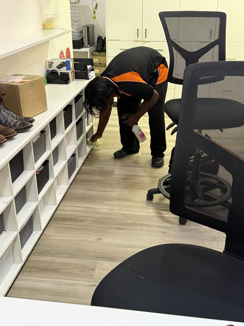 Cleaner wiping white office shelving with spray cleaner beside desk chairs