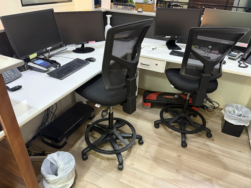 Office desks with monitors and two mesh drafting chairs on a timber-look floor