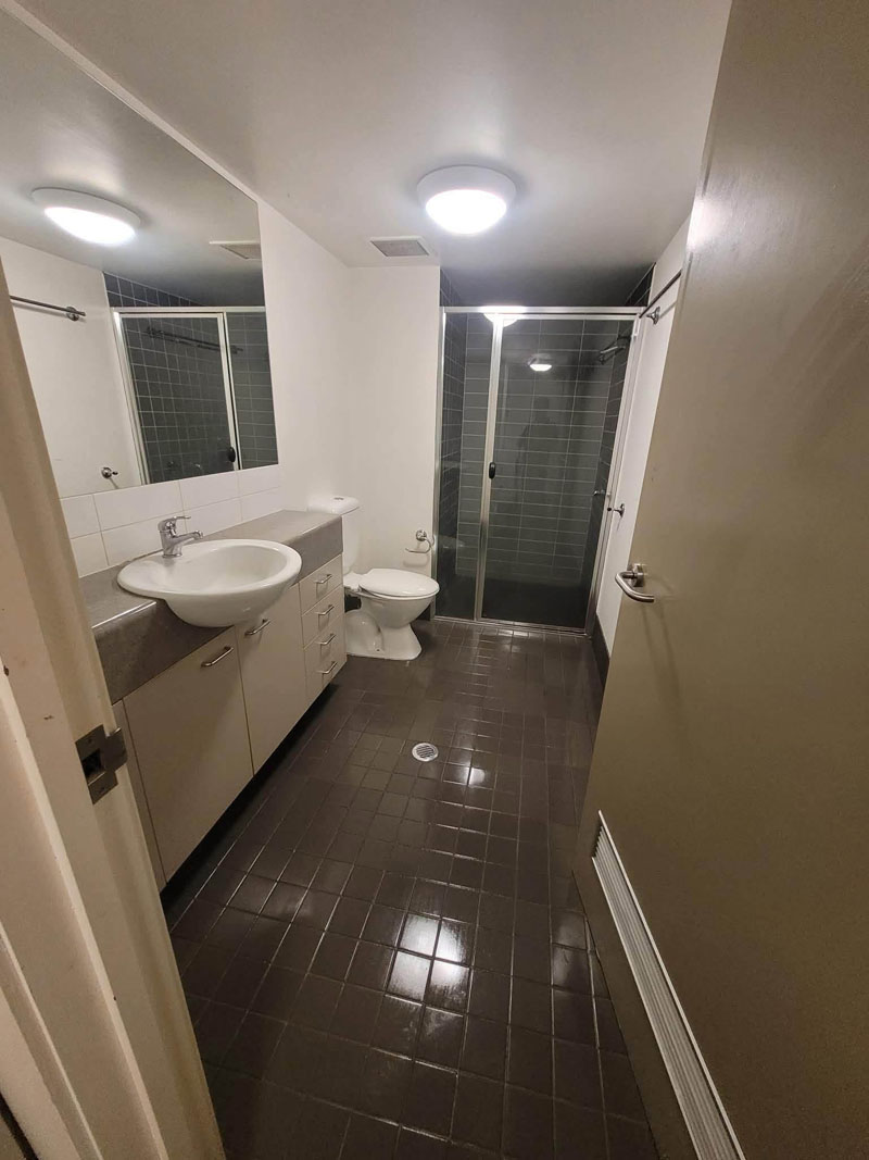 Bathroom with shiny dark floor tiles, vanity, toilet and shower