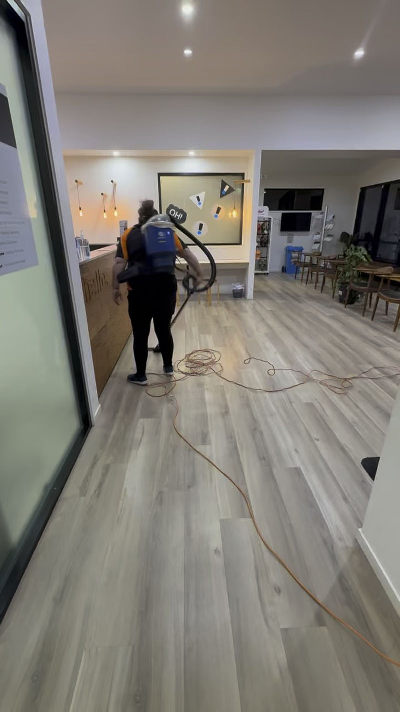 Cleaner with a backpack vacuum on a timber-look floor in an open-plan office