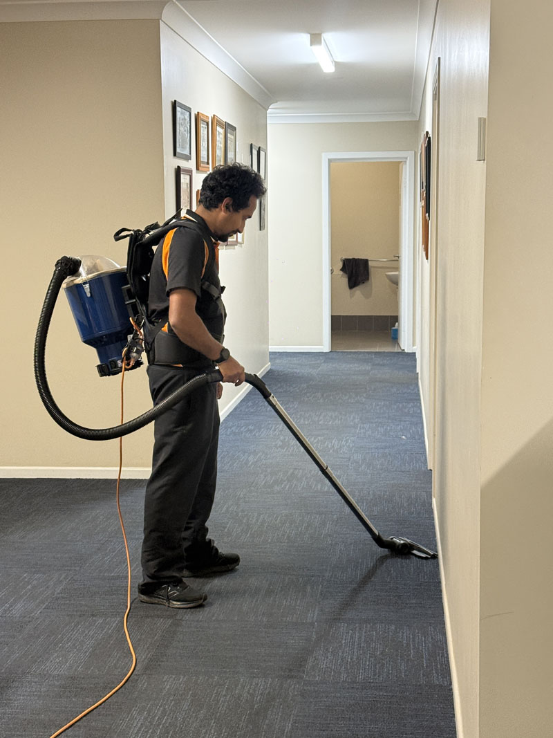 Cleaner vacuuming a carpeted office hallway with a backpack vacuum