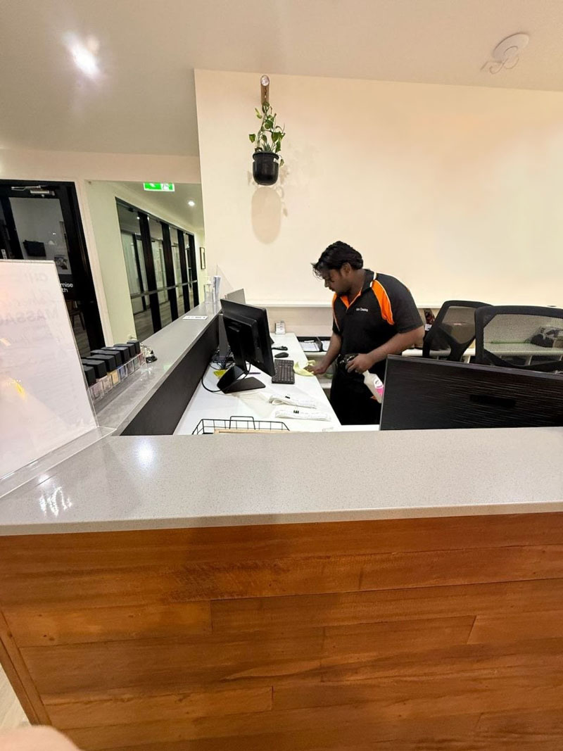 Cleaner wiping down a reception desk with spray cleaner in an office foyer